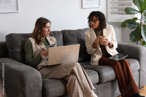 Canvastavla Diverse women colleagues sitting on sofa in lounge, using laptop, tablet and mug