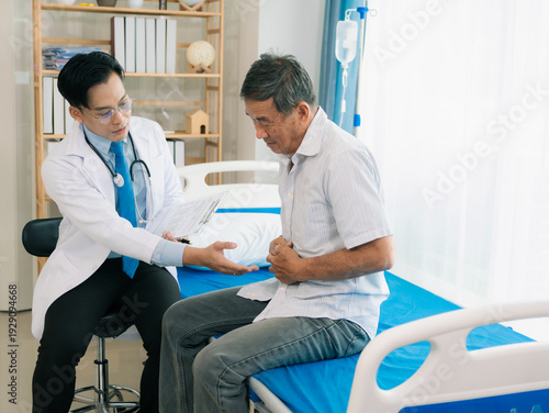 An Asian male doctor and an elderly male patient are discussing stomach pain from poisoning while sitting on a bed in a health concept clinic.
