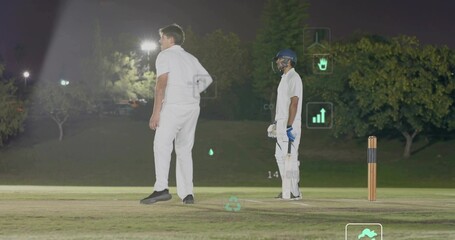 Standing two cricketers holding bat, wearing navy helmet, white kit on night pitch with AR icons