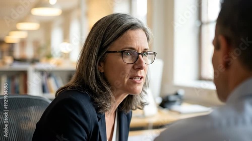 Professional Woman in Glasses Engages in Serious Conversation in Modern Office, Highlighting Focused Communication and Collaboration for Effective Outcomes