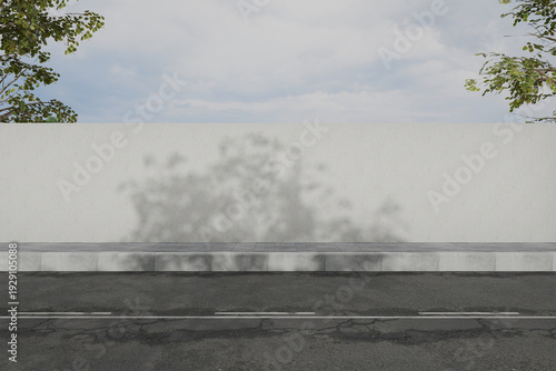 A gray wall with a tree shadow on it stands behind a road curb with a tree on each side