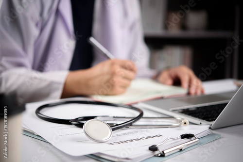 doctor hands writing on medical document with stethoscope and health insurance claim form on desk. Concept of healthcare coverage, life insurance policy and medical protection.
