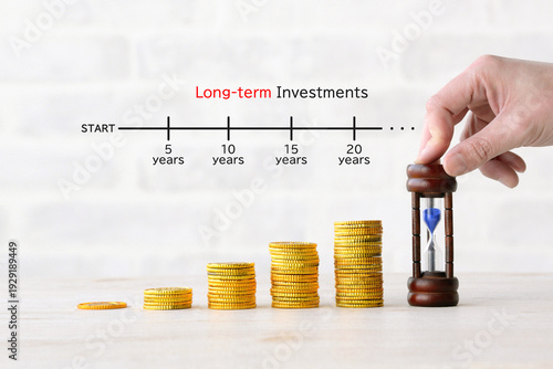 積み上げられた硬貨と砂時計を置く人物の手―長期投資イメージ