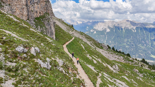 Aerial, bird view, hiking trail with some hikers, tourists along a mountain slope with grass and rocks,  near Rotwandhütte, Rifugio Roda di Vaèl mountain hut in Italian Dolomites. Beautiful hiking des