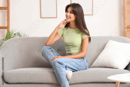 Dreaming young woman sitting on sofa at home
