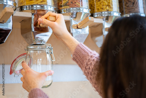 Woman refill glass jar with dry groceries from dispenser at zero waste store, promote sustainable lifestyle, eco-friendly shopping, reduce plastic use and protect environment