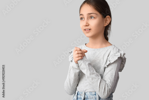 Little girl praying on grey...