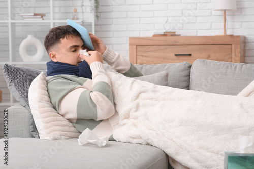 Foto Ill young man with hot water bottle and tissue sneezing on sofa at home