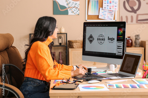 Young female graphic designer working with tablet and computer at table in of...