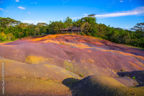 Multicolored sand dunes at Chamarel Seven Colored Earth Geopark with a wooden lodge nestled among trees of a tropical jungle in Mauritius, Africa.