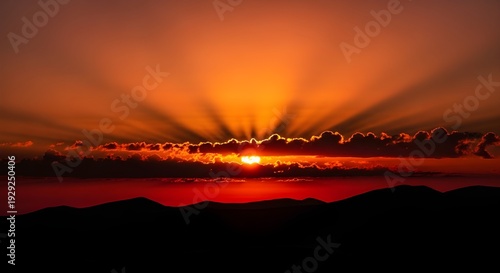 Dramatic sunset with radiant crepuscular sun rays over silhouetted mountains and clouds, warm sky