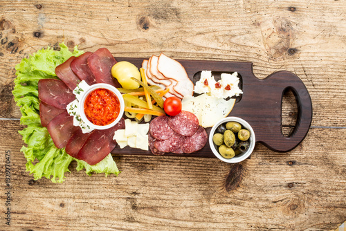 A rich wooden board with appetizers, on which various cured meats, cheeses, olives, ajvar and fresh salad were served.