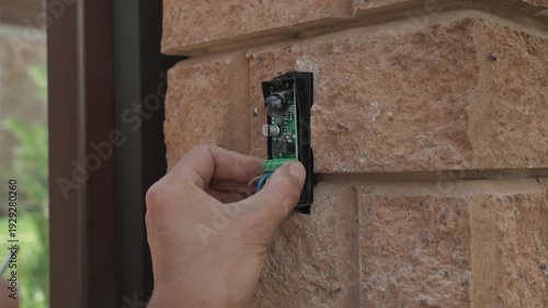 Close-up of a technician's hands using a screwdriver to tighten contacts on an infrared safety sensor during gate automation setup