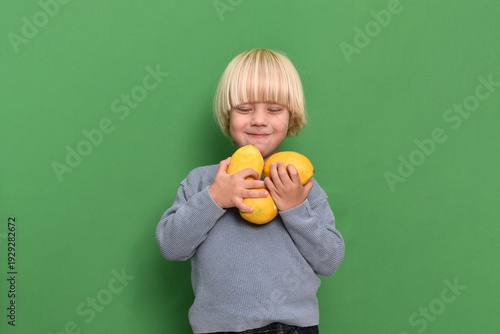 Little boy holding fresh lemons against green background, concept of healthy nutrition, vitamin C, immunity support and virus prevention. Child promoting natural food and strong immune system 