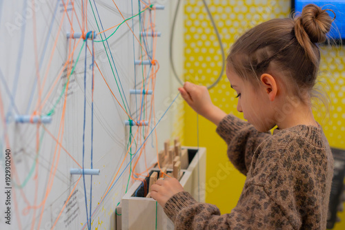 Young girl interacting with a colorful string and peg display at an interactive museum exhibit, engaged in a hands-on learning experience with educational tools