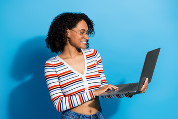 Young chic woman with curly hair using a laptop against a blue background smiling and stylish