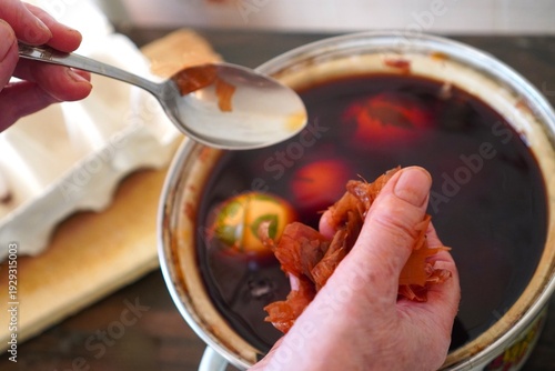 Elderly woman's hands holding vintage silver spoon and onion peel over retro pan with red eco-friendly onion peel solution with easter eggs for painting for the holiday