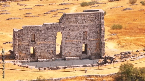 Cinematic 4K drone shot of the ancient Roman theater of Acinipo archaeological site, showing the standing stone wall and seating area in the mountains near Ronda, Malaga province.