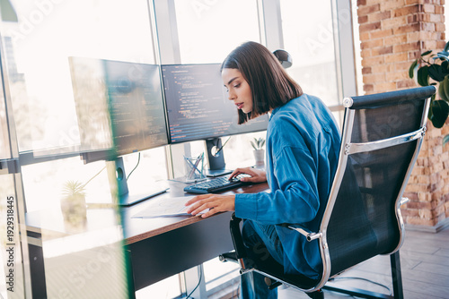 Tableau sur toile Businesswoman coding at a modern loft office with dual monitors and a focused fr