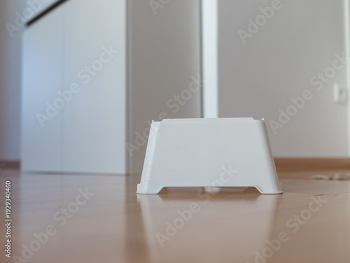 Minimalist white plastic step stool for children on a wooden floor. Modern anti-slip toddler step in a bright, clean home interior.