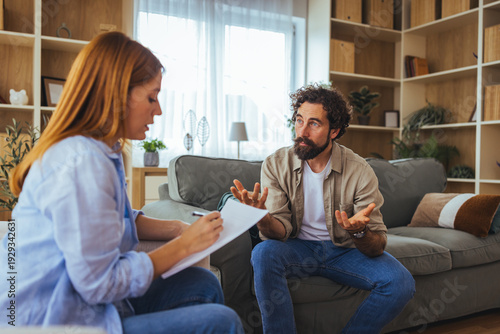 Photos Man in Therapy Session Talking With Female Counselor On Couch In Home Counseling