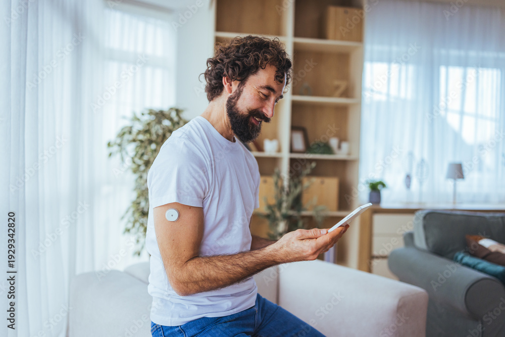 Fototapeta premium Man Using Smartphone to Check Glucose Monitor at Home, Managing Diabetes With Wearable Sensor