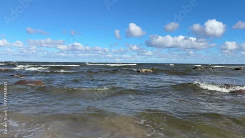 Waves moving toward sandy shore under soft clouds. Natural sea ambience recorded outdoors. Clear 4K coastal video.