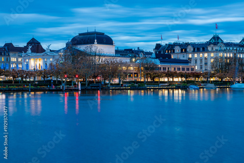 Beautiful blue hour in Autumn over Lake Zurich seen from a floating pier with views over the Swiss Alps and the lakeside of the city with the famous theatre and other historical buildings