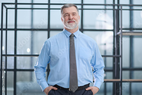 A man in a suit and tie is standing in front of a window, looking thoughtful