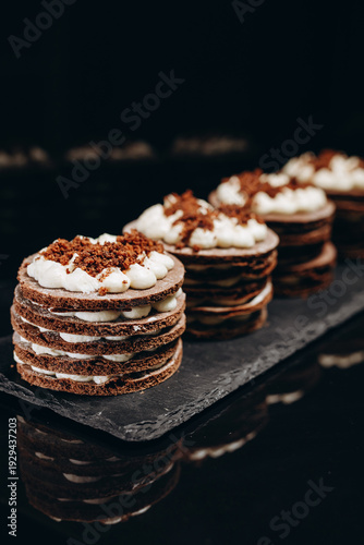 Individual layered chocolate cream desserts on slate board, gourmet mini cakes for bakery display