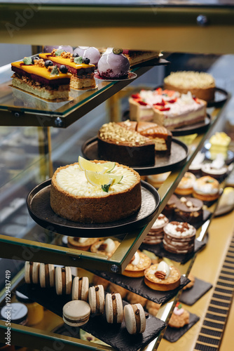 Assorted gourmet cakes and pastries displayed in a glass bakery case with macarons and tarts