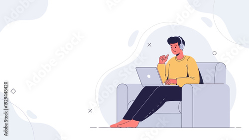 Young man listening to music on headphones and working on laptop while sitting on sofa