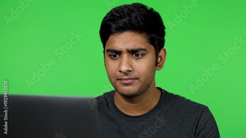Young Indian man focused on a laptop screen against a green backdrop