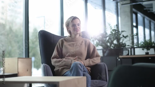 A woman is sitting in a chair in a room with a potted plant in front of her