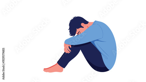 Depressed and lonely young man sitting on the floor with his head down and arms wrapped around his knees in a state of despair.