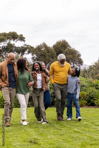African American family with senior, teenage and child walking across lawn in park wearing sweaters
