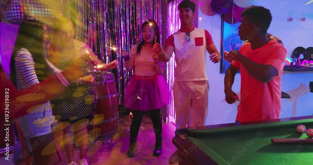 Fototapeta premium Holding sparklers, seven friends in party clothes celebrating in party room with pool table