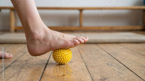 Foot massage with spiky ball on wooden floor for physical therap and ankle recovery exercise to relieve pain and improve mobility