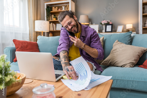 Freelance AI consultant working from home on sofa, smiling during phone call while reviewing analytics reports on laptop, remote technology advisory and innovation strategy session