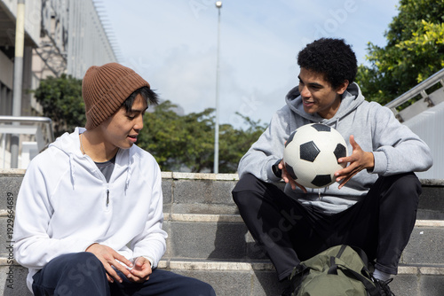 Foto Diverse teenage male friends sitting on concrete steps holding soccer ball and g