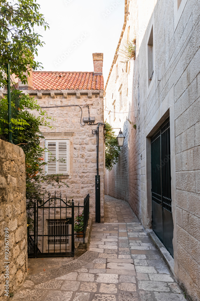 Fototapeta premium Scenic narrow stone street and medieval limestone walls in Dubrovnik Old Town at sunrise, Croatia. Historic Mediterranean architecture, ancient fortress view with Adriatic sea on background.