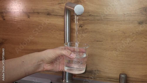 A man fills a glass with water from a tap, a close-up of his hand holding a glass