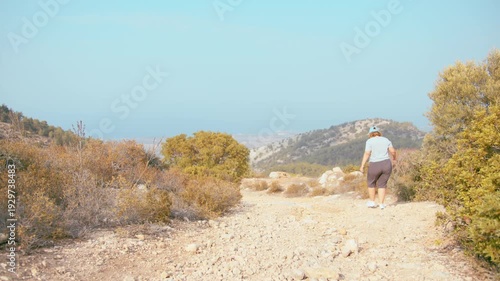 Woman Hiking Through Rocky Mountain Landscape Under Bright Sunlight on Clear Summer Day