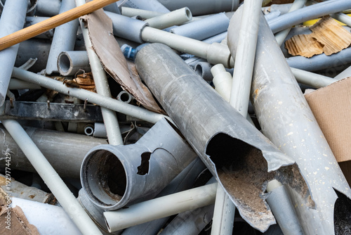 A tangled heap of various gray plastic pipes and plumbing tubes lies at a waste container. Construction site material renovation concept. Broken connectors and damaged tubing