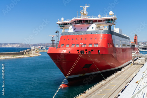 Large red and white cruise ferry docked at the industrial port of Marseille, France, under a clear blue summer sky.