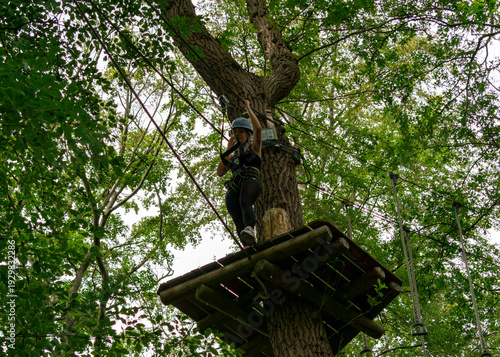 Canvastavla Young woman stepping forward on treetop platform in adventure park