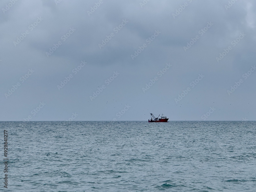 Fototapeta premium Fishing vessel at sea on a cloudy day, bobbing gently in the water