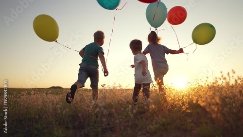 Happy children run in summer park with colorful balloons. sane child runs across grass in green summer park. Multi-colored funny balloons in hands of child. group of children run at sunset.