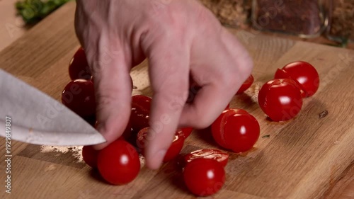 A chef cuts tomatoes into halves for a salad on a cutting board with a knife.