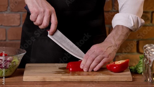 A cook cuts red bell peppers into pieces for a salad with a knife.